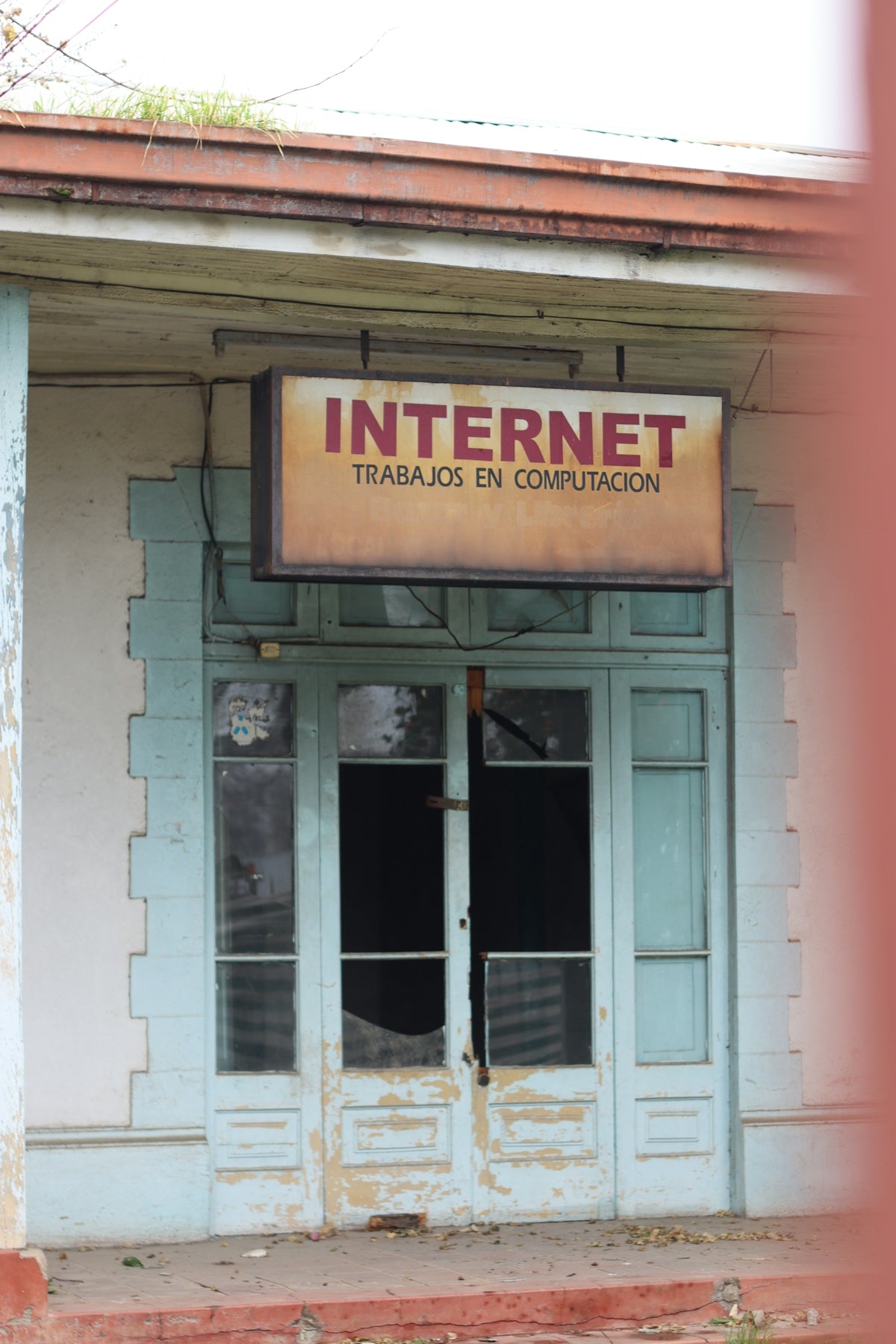 Old, broken door reads internet and trabajos en computación.