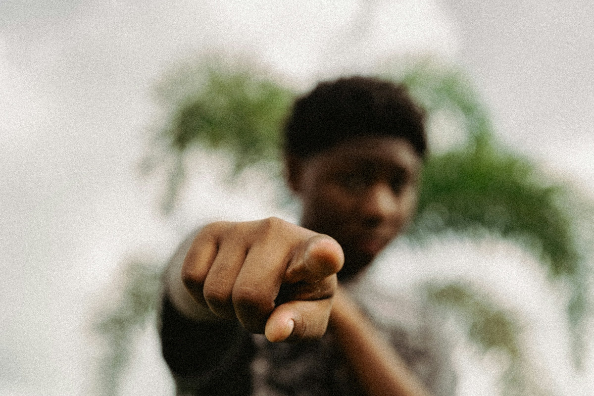 A person pointing forward with a blurred palm tree in the background